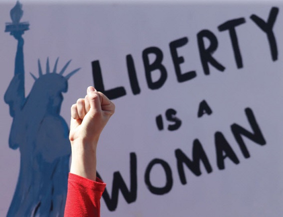 Woman's fist raised before a sign reading 'Liberty is A Woman'