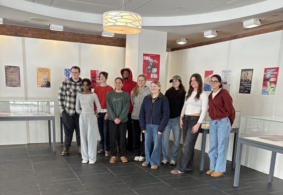 Students gathered in front of the exhibit they curated, with wall-hung posters and exhibit cases of materials behind them.